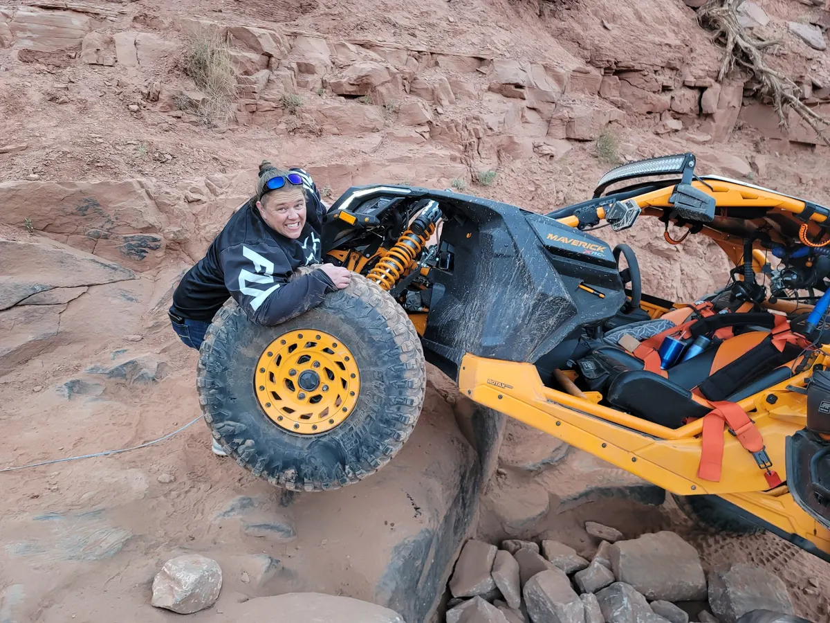 A rider changing a wheel on a Can-Am Maverick X RC out on red rock